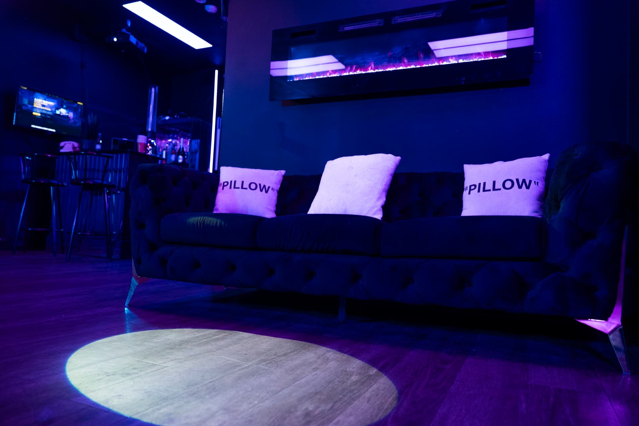 The lounge at Lush Event Space — velvet sofa beneath the fireplace wall in violet light